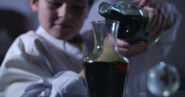 Siyah ve kırmızı kimyasal reaksiyonların yakın plan yüzü. Küçük kıvırcık saçlı beyaz çocuk arka planda bulanıklaştı. Zeka, kimya, nesil Z. Cinema 4k Prores Hq.