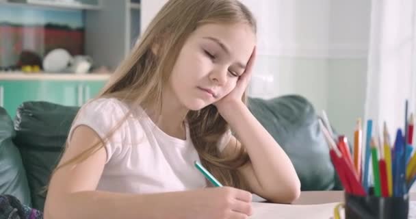 Een slapend blank meisje aan tafel met een pen in één hand. Schattig uitgeput schoolkind dat wakker wordt en huiswerk blijft maken. Overwerken, studeren, onderwijs. Bioscoop 4k Prores Hq. — Stockvideo