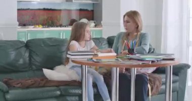 Anne, kızını masada otururken eğitiyor. Huzursuz çocuğun ev ödeviyle ilgili sorunları var. Ebeveyn çocuğuna derslerinde yardım ediyor. Eğitim, öğrenme, öğrenim kavramı. Sinema 4k Prores Merkezi.