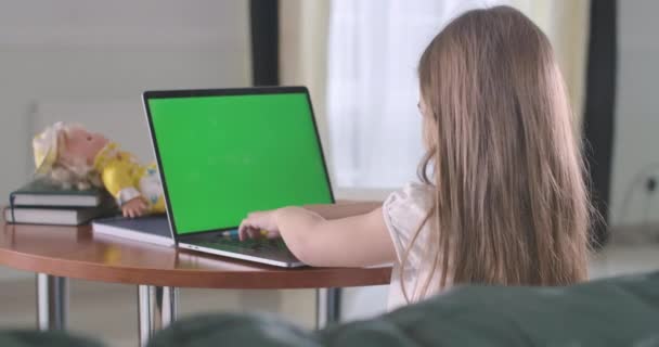 女生在带有绿色屏幕的笔记本电脑上打字的背侧视图。 在网上学习或使用社交媒体的白人儿童。 电子学习，在线，互联网，教育，游戏，成瘾。 电影4k Prores Hq. — 图库视频影像