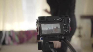 Ön planda duran video kameranın yakın çekimi, arka planda oturan ve el sallayan olgun beyaz kadın. Kıdemli blogcu çevrimiçi yayına başlıyor. Teknolojiler, blog yazma, medya.