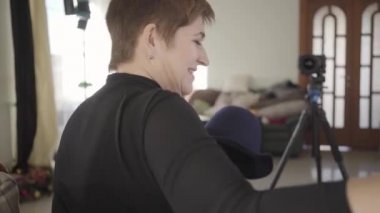 Beyaz kadın, kısa saçlı, önünde duran zarif şapkasını kameraya gösteriyor. Yetişkin kadın blogcu blogu için video kaydediyor. Modern teknolojiler, çevrimiçi, blog yazma.