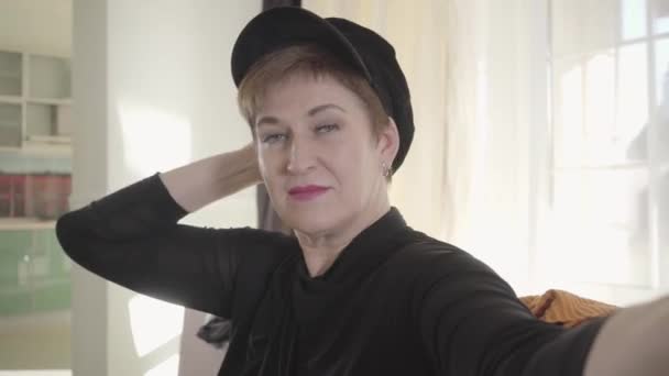 Close-up portrait of beautiful Caucasian woman in elegant hat looking at camera and smiling. Senior blogger recording selfie video about fashion. Technologies, blogging, social media. — Stock Video