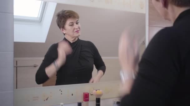 Reflection of happy Caucasian mature woman adjusting her elegant outfit and hair in front of big mirror. Cheerful senior good-looking lady satisfied with her appearance. Fashion, aging, happiness. — Stock Video