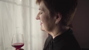 Camdan dışarı bakıp kırmızı şarap içen kendine güvenen beyaz iş kadınının portresi. Güneş ışığının altında duran olgun, zarif bir bayan. Kendine güven, dinlenme. Boş zaman.