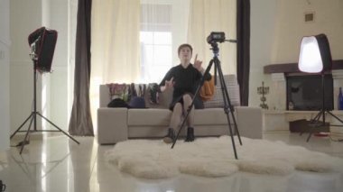 Yetişkin, esmer, beyaz bir kadının moda detaylarını kameraya açıklarken orta boy fotoğrafı. Son sınıf öğrencisi kadın renkli bir eşarp takıyor ve video kameraya bakıyor. Blogger video kaydı. Modern teklojiler.
