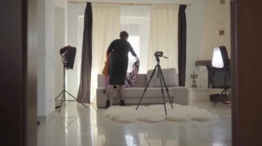 Kameraların önünde renkli eşarplar seren beyaz bir kadının arka görüntüsü. Olgun kadın blogcu video kaydı için hazırlanıyor. Çevrimiçi, canlı, günlük.