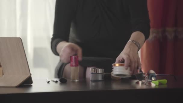 Gros plan des mains féminines caucasiennes qui mettent des produits de maquillage sur la table. Femme méconnaissable se préparant à appliquer le maquillage. Mode, beauté, soin du visage, soin de la peau . — Video
