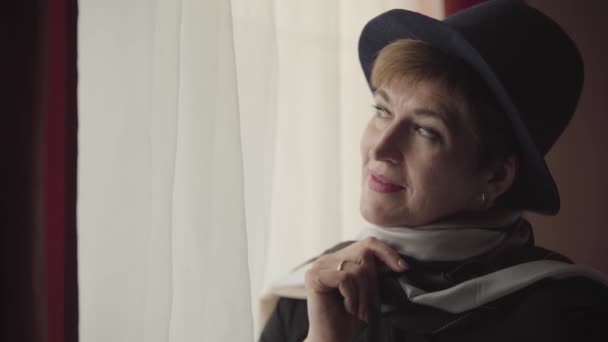 Close-up face of thoughtful Caucasian woman in stylish hat and scarf looking out the window. Portrait of beautiful confident retiree thinking. — Stock Video