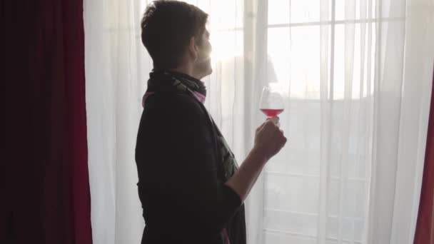 Mujer caucásica mirando por la ventana por la noche. Sonriente dama caucásica degustación de vino tinto de vidrio. Descanso, ocio, alcohol . — Vídeos de Stock