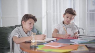 Kafkasyalı çocuk kafası masanın üzerinde yatıp uyuyakalmış. İkiz kardeşi onu uyandırdı. Kardeşler evde birlikte okuyorlar. Eğitim, zeka, yorgunluk, Z kuşağı.