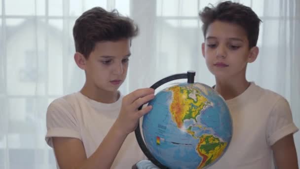 Dos hermanos gemelos caucásicos mirando el globo y hablando. Hermanos estudiando juntos en casa. Educación, geografía, inteligencia . — Vídeo de stock