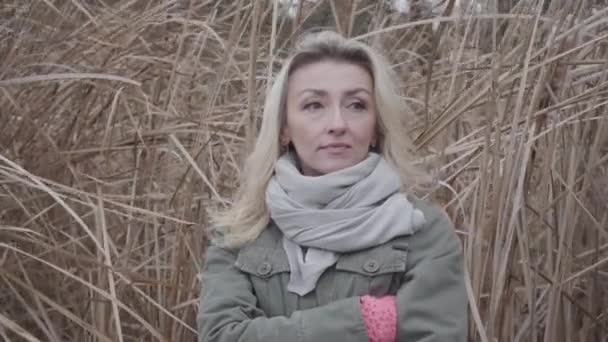 Close-up of sad Caucasian woman standing at the background of yellow autumn bushes. Charming girl with blond hair and brown eyes waiting outdoors. — ストック動画