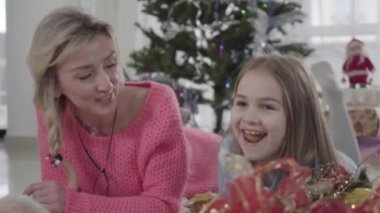 Kafkasyalı bir kız ve kadının yerde yatıp konuştuğu yüzler. Neşeli sarışın anne esmer kızıyla eğleniyor. Mutlu bir aile Noel ağacının arkasında dinleniyor..