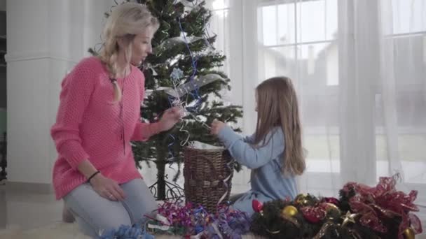 Mujer bastante caucásica hablando con la niña y tomando la decoración de Navidad. Feliz madre ayudando a su hija a elegir decoraciones antes de Navidad . — Vídeo de stock