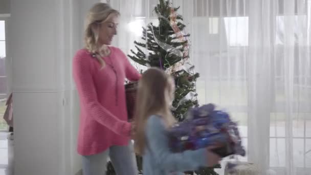 Hermosa madre rubia caucásica y su hija morena entrando a la habitación con decoración para el árbol de Año Nuevo. Mujer preparándose para la Navidad con su hijo. Casa de decoración familiar para la celebración . — Vídeo de stock