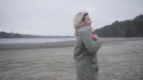 Mujer rubia caucásica alegre girando en la orilla del lago o el río. Chica feliz divirtiéndose al aire libre . — Vídeo de stock