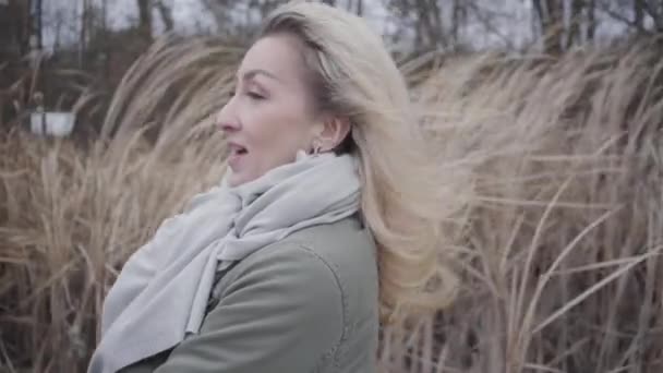 Seitenansicht attraktiver junger Frau, die im Wind steht. blondes kaukasisches Mädchen genießt grauen Herbsttag im Freien. — Stockvideo