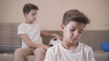 Tatlı beyaz çocuk ön planda oturan ikiz kardeşine egzersiz kitabı veriyor. Kardeşler evde ödev yapıyor. Öğrenciler tablet ve not defteri kullanarak çalışıyor.