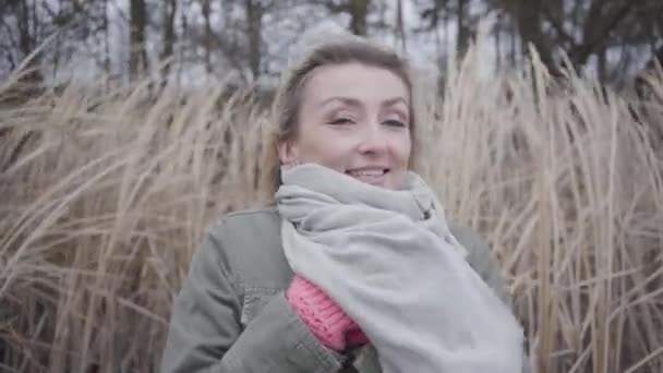 Retrato de una joven mujer hermosa de pie en el viento frío. Encantadora chica con cabello rubio y ojos marrones esperando al aire libre. Cámara moviéndose de derecha a izquierda . — Vídeo de stock