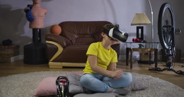VR 구글에서 코카서스 소년을 웃으며 카펫에 앉아 그 의 몸을 움직이는 모습. 집에서 증강현실 헤드셋을 사용하는 행복 한 학생. 영화 4K 프로 데스 HQ 세대. — 비디오