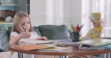 Küçük tatlı beyaz kız evde matematik yapıyor. Güzel çocuk egzersiz kitabına figürler yazıyor ve düşünüyor. Zeka, eğitim, öğrenim. Sinema 4k Prores Merkezi.
