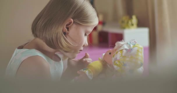 Вид сбоку на маленькую белую девочку, играющую с куклой. Серьезный блондинка в элегантном платье проводит выходные в своей комнате дома . — стоковое видео