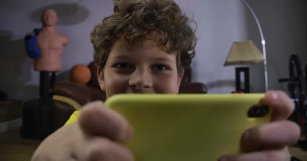 Visage de mignon garçon caucasien avec les yeux fatigués se mettre en colère comme perdre dans le jeu vidéo. Adolescent aux cheveux bouclés en T-shirt jaune utilisant un smartphone pour jouer. Jeux, technologies. Siège social Cinema 4k ProRes . — Video