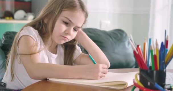 Masada oturup ödev yapan yorgun, beyaz bir kız. Yorgun çocuk, egzersiz kitabının üzerine uzanıp gözlerini kapatıyor. Çok çalışmak, okumak, eğitim kavramı. Sinema 4k Prores Merkezi. — Stok video