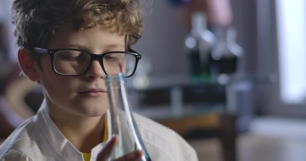 Portrait d'un garçon caucasien tenant une fiole avec du liquide bleu et réfléchissant. Gros plan d'un adolescent intelligent qui expérimente des réactifs chimiques. Siège social Cinema 4k ProRes . — Video