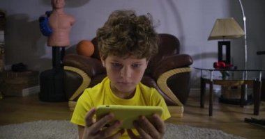 Akıllı telefon ekranına bakıp gülümseyen kıvırcık saçlı sevimli çocuğun yakın plan portresi. Beyaz çocuk çevrimiçi çizgi film izliyor. Sosyal medya, internet, modern teknolojiler. Sinema 4k Prores Merkezi.
