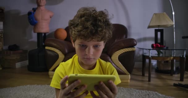 Detailní portrét půvabného kudrnatého chlapce, jak se dívá na obrazovku smartphonu a usmívá se. Kavkazské dítě sledovat karikatury online. Sociální média, internet, moderní technologie. Cinema 4k Prores Hq. — Stock video