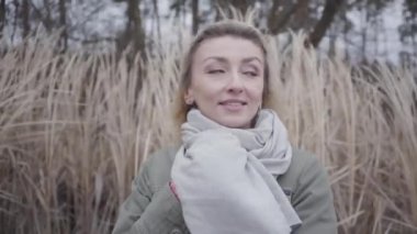 Soğuk rüzgarda dikilen kahverengi gözlü, güzel, beyaz bir kadının yakın çekimi. Dışarıda bekleyen çekici sarışın kız. Kamera soldan sağa hareket ediyor.