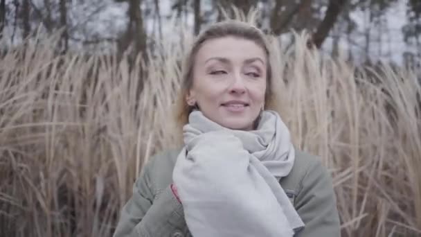 Cara de cerca de la joven hermosa mujer caucásica con ojos marrones de pie en el viento frío. Encantadora rubia esperando al aire libre. Cámara moviéndose de izquierda a derecha . — Vídeo de stock