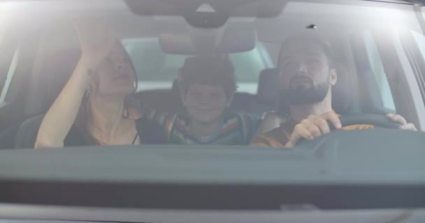 Маленький белый мальчик с вьющимися волосами сидит в автосалоне с родителями. Молодая семья выбирает новый автомобиль в аренду или для покупки вместе. Автосалон, автобизнес. Съемки в кинотеатре 4k . — стоковое видео