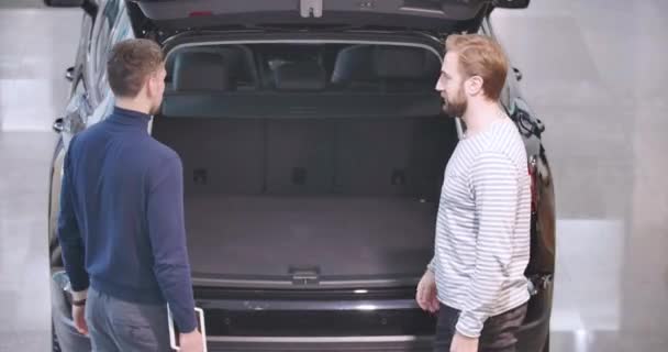 Vista trasera de dos hombres caucásicos de pie frente a un camión y estrechando las manos. Comerciante y cliente haciendo trato en sala de exposición. Negocio de coches, alquiler de coches, concesionario de coches. Cinema 4k metraje ProRes HQ . — Vídeos de Stock