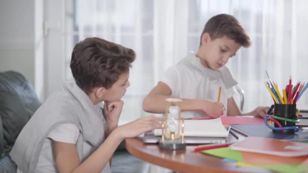 Vista laterale del piccolo ragazzo caucasico in attesa del fratello gemello per disegnare il quadro e dare il cinque. Fratelli intelligenti che fanno i compiti insieme a casa. Generazione Z, mente brillante, concetto di istruzione . — Video Stock