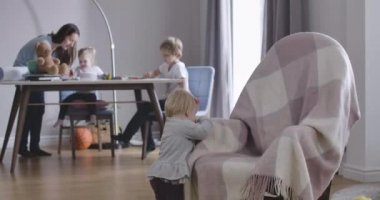 Kafasında kırmızı kurdele olan güzel sarışın kız sallanan sandalyenin arkasından oyuncak kaldırıyor. Onun güzel annesi, kız kardeşi ve erkek kardeşi arka planda masada oturuyormuş gibi konuşuyorlar. Sinema 4k Prores Merkezi.