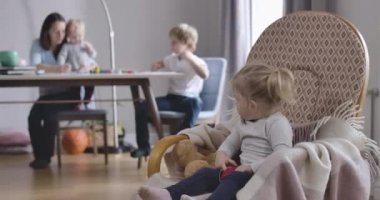 Kafkasyalı konsantre olmuş sarışın kızın portresi büyük ailesine bakıyor arka planda oturuyor ve oyuncaklarla oynamaya devam ediyor. Sallanan sandalyede oturan tatlı çocuk. Sinema 4k Prores Merkezi.