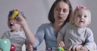 İki kızıyla oyuncak oynayan mutlu esmer beyaz kadın portresi. Sevimli pozitif kız bebekler günlerini anneleriyle geçirirler. Sinema 4k Prores Merkezi.