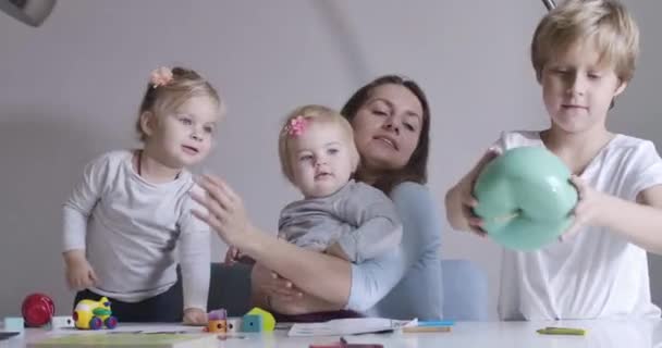 Portret szczęśliwej rodziny spędzającej razem dzień w domu. Młoda brunetka matka rozmawia z synem trzymając duże jabłko zabawki, córki bawiące się zabawkami. Kino 4k Prores Hq. — Wideo stockowe