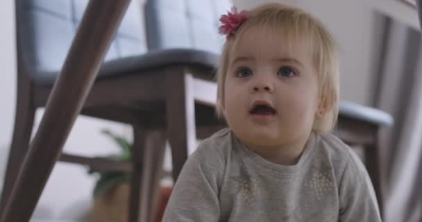 Portrait de charmante petite fille caucasienne aux yeux gris et aux cheveux blonds regardant loin avec la bouche ouverte. Portrait d'un enfant charmant caché sous la table. Siège social Cinema 4k ProRes . — Video