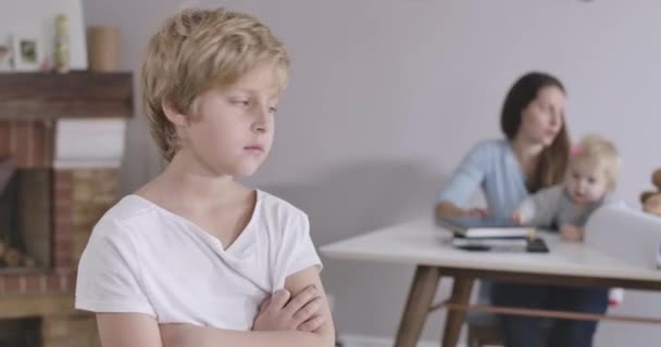 Gros plan d'un garçon caucasien triste aux yeux gris regardant en arrière sa sœur et sa mère, se retournant et regardant ailleurs. Un type en T-shirt blanc posant à la maison. Siège social Cinema 4k ProRes . — Video