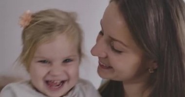 Kafkasyalı mutlu anne ve kızın yakın çekim yüzleri eğleniyor. Genç esmer kadın ve küçük sarışın kız gülüyor. Anne çocuğuna bakıyor. Mutluluk, rahatlık, olumluluk. Sinema 4k Prores Merkezi.