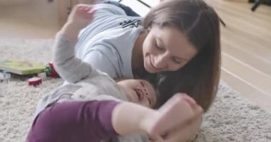 Kızıyla oynayan mutlu esmer annenin portresi. Küçük bir kızla yumuşak halıda yatan ve gülen bir kadın. Mutluluk, rahatlık, annelik sevinci. Sinema 4k Prores Merkezi.