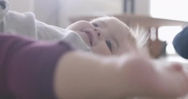 Linda niña alegre acostada en una alfombra suave en casa y sonriendo. Retrato de un hermoso niño caucásico a la luz del sol. Sede del cine 4k ProRes . — Vídeo de stock