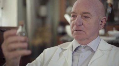 Şişeye sıvıyla bakan ağlayan yaşlı adamın yakın plan yüzü. Beyaz cüppeli olgun beyaz eczacı hayat kurtarmayı başaramadı. Antika eczanede depresif yalnız bir adamın portresi..