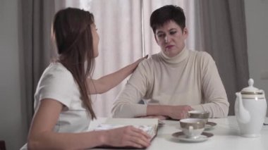 Genç esmer kız yaşlı kadını sakinleştiriyor. Yetişkin kız annesiyle fotoğraf albümü izliyor. İki kadın anıları topluyor..