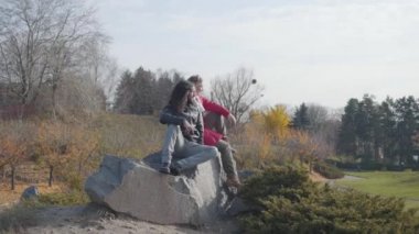 Sarışın, beyaz bir kadın hippi Orta Doğulu sevgilisiyle kayaların üzerinde oturuyor ve konuşuyor. Mutlu çift sonbahar parkında dinleniyor. Dışarıyla çıkan kaygısız insanlar..