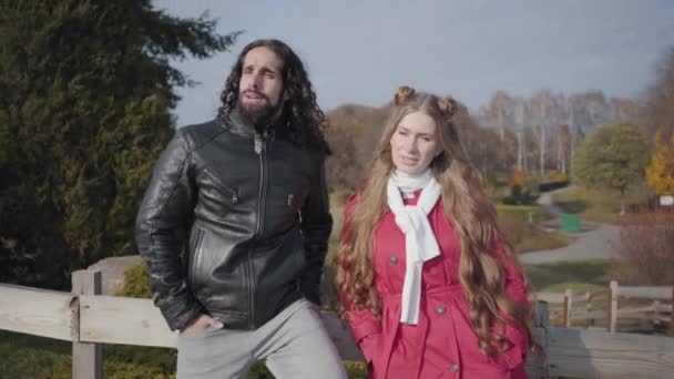 Joven hombre de Oriente Medio con el pelo rizado largo hablando con su novia rubia caucásica en el parque de otoño. Pareja feliz disfrutando del día soleado al aire libre. Citas, unión, unión, felicidad . — Vídeos de Stock